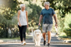 An older couple walk their dog in the park, boosting their physical, emotional, and brain health by exercising.